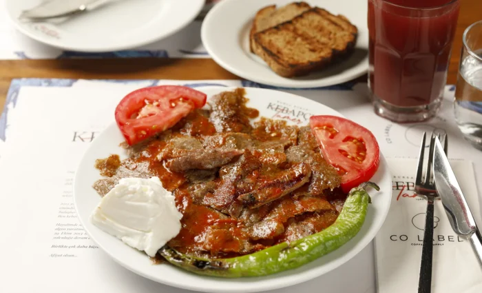 Kebapçı Tamer'de servis edilen, tırnak pide üzerinde yaprak döner, özel domates sosu, tereyağı ve yanında yoğurt ile sunulan 1 porsiyon geleneksel Bursa Kebabı.