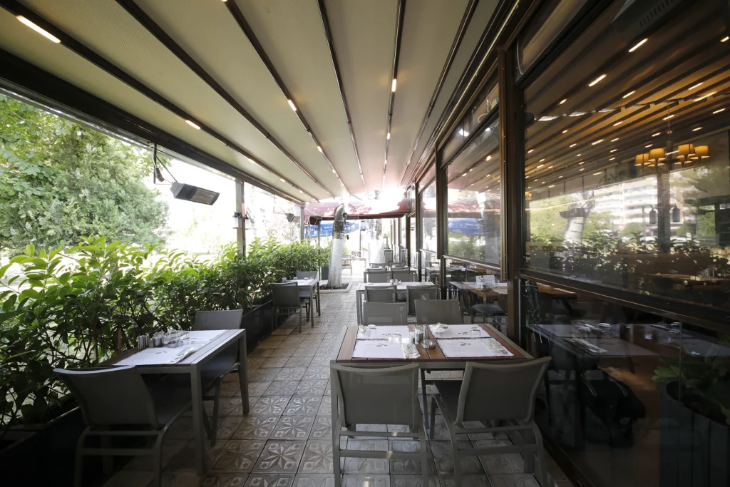 Kebapçı Tamer restoranının, sol tarafında Üç Fidan Parkı'nın yeşil manzarası görünen, tente gölgeli masalara sahip açık hava bahçe bölümü.